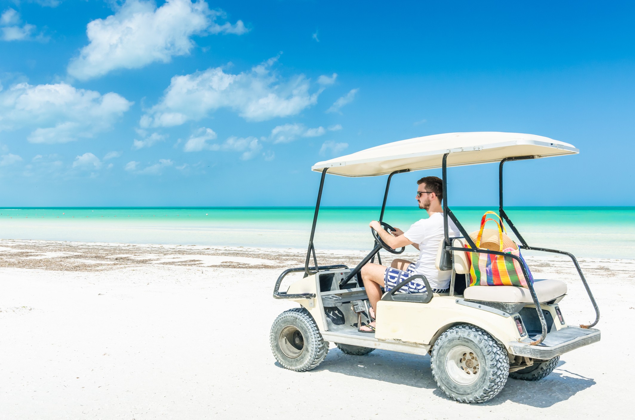 Cómo llegar a Holbox: Imagen de un hombre en un carro de arena, caminando por la playa.