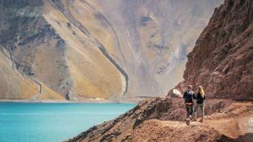 Pareja observando un mar de aguas cristalinas y montañas en el Cajón del Maipo.