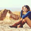 Mujer sentada sobre rocas frente al mar usando botas marrones y blusa azul