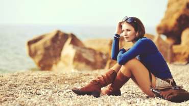 Mujer sentada sobre rocas frente al mar usando botas marrones y blusa azul