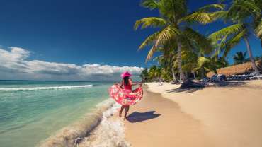 Mujer caminando descalza sobre la arena del Caribe frente al mar.