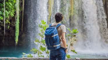 Hombre de espaldas con mochila observando la vista de una cascada