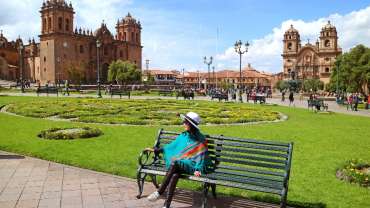 Mujer sentada en un banco frente a un sitio turístico en Perú