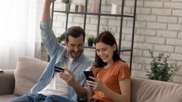 Pareja sosteniendo una tarjeta de crédito, celebrando la compra de un boleto barato desde el celular.