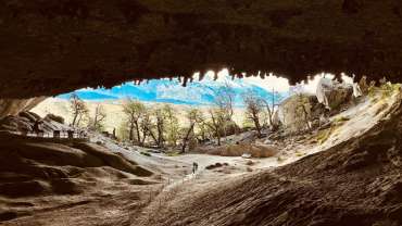Dos personas saliendo de la Cueva del Milodón frente a árboles y montañas.