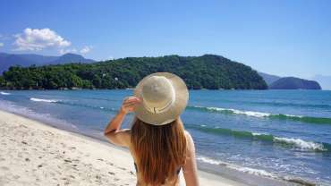 Mujer de espaldas observando la playa de Ilhabela con un sombrero en la cabeza