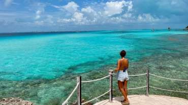 Mujer observando el mar con aguas cristalinas en un día soleado
