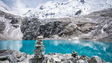 Imagen de paisaje con montañas y un lago azul cristalino con algunas rocas apiladas