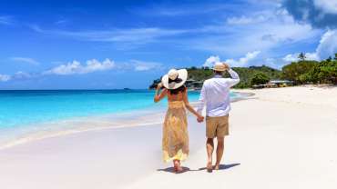 Pareja caminando por la playa de la mano con vista a aguas cristalinas
