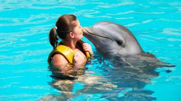 Mujer dentro de las aguas de Punta Cana dando un beso a un delfín