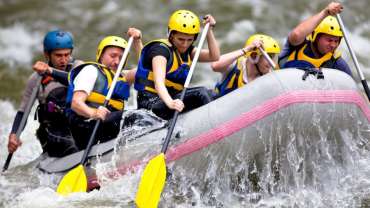 Grupo de personas blancas dentro de una canoa, remando en un río.