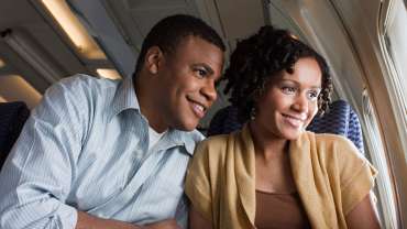Pareja heterosexual dentro de un avión observando la vista con una sonrisa en el rostro