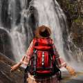 Mujer con mochila en la espalda posando para una foto frente a una cascada