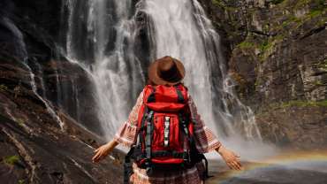 Mujer con mochila en la espalda posando para una foto frente a una cascada