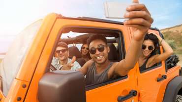 Grupo de amigos dentro de un mini auto naranja posando para una selfie