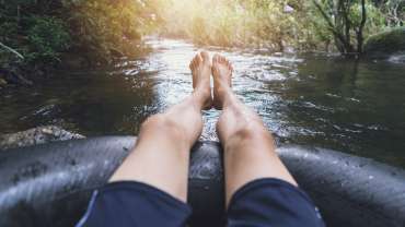 Hombre con los pies fuera del flotador practicando tubing en un río