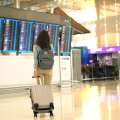 Mujer sosteniendo una maleta frente al panel del aeropuerto.
