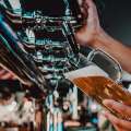 Persona sirviendo cerveza dorada en un vaso grande desde un grifo en un bar.