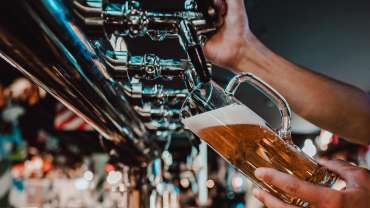Persona sirviendo cerveza dorada en un vaso grande desde un grifo en un bar.