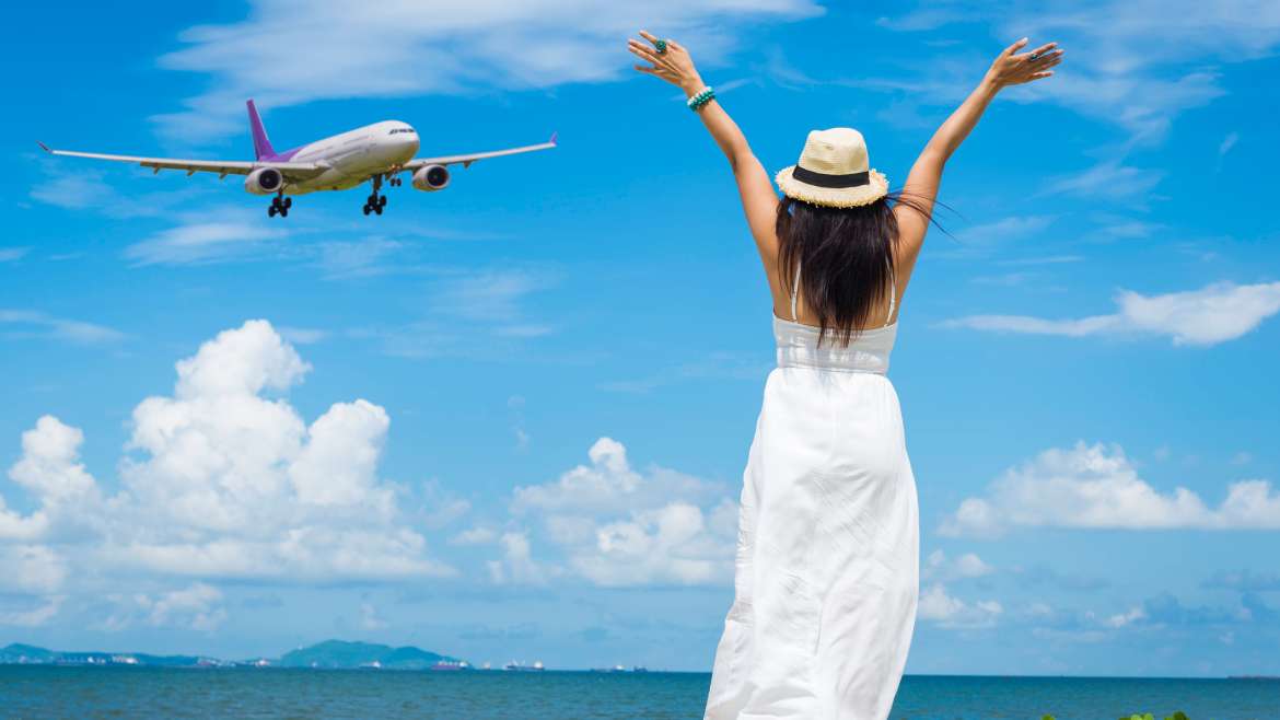 Mujer en la playa con los brazos abiertos y un avión frente a ella.