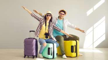 Pareja animada sentada encima de la maleta de viaje.