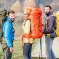Tres excursionistas con mochilas grandes posan al aire libre junto a una tienda de campaña.