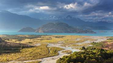 Paisaje patagónico con río turquesa, montañas nevadas y cielo nublado.